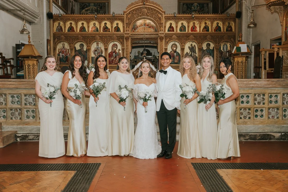  Bride and groom with bridesmaids inside the ornate interior of Saint Nectarios Church following their Greek Orthodox wedding in Battersea. 
