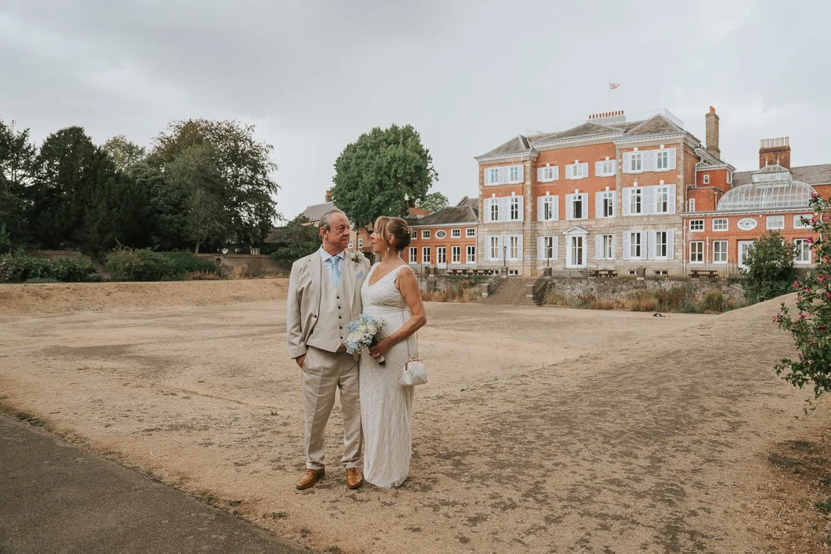 Bride and groom standing together in the grounds with York House, Twickenham, in the background during their outdoor wedding portraits. 
