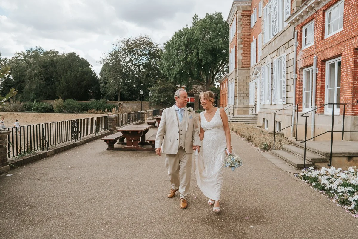  Newly married couple laughing together as they walk outside the historic York House in Twickenham after their wedding ceremony. 