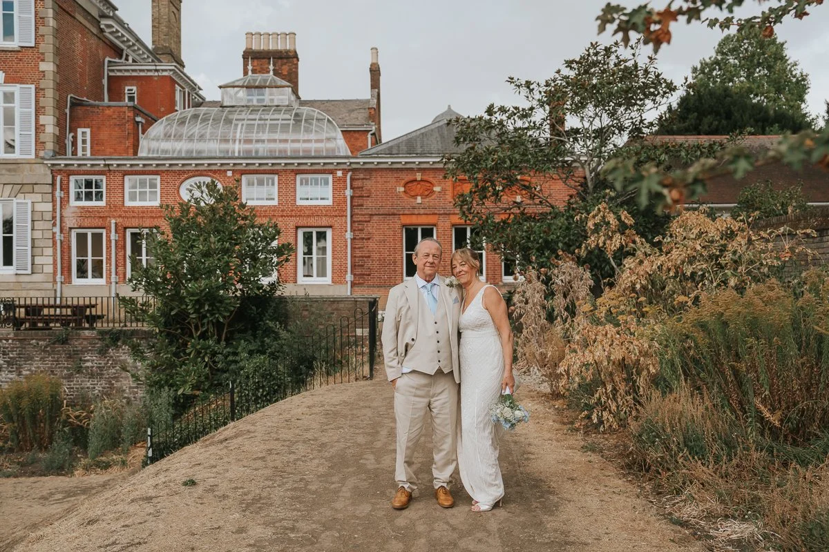  Bride and groom posing together in the gardens with the red-brick exterior of York House, Twickenham, providing a beautiful backdrop for their wedding portraits. 