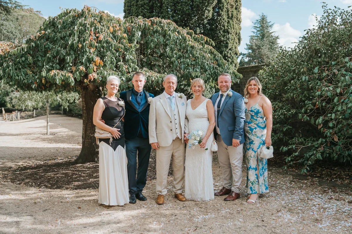  Family group photograph with the bride and groom in the gardens at York House in Twickenham following their wedding ceremony. 