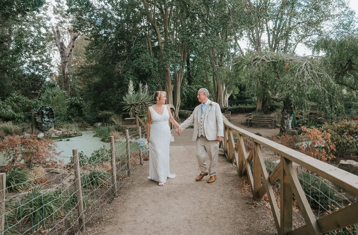  Bride and groom walking hand in hand through the beautiful gardens at York House, Twickenham, during their relaxed wedding photography session. 
