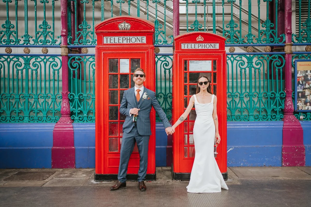  Bride and groom beside traditional red telephone boxes at Smithfield Market during their Balfour St Barts wedding photography. 