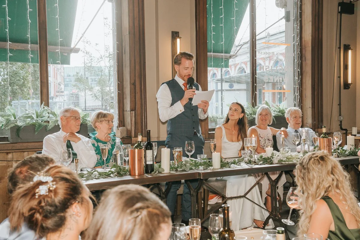   Groom giving his wedding speech beside the bride at Balfour St Barts in Smithfield, London.  