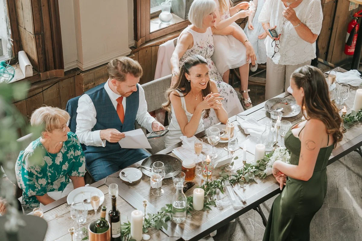  Bride chatting and laughing with wedding guests at the top table inside Balfour St Barts. 