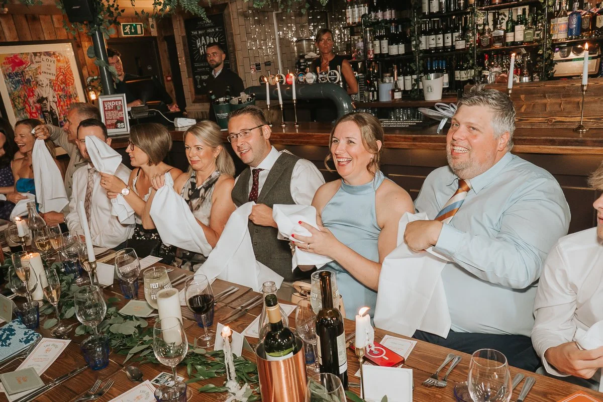  Guests waving napkins and laughing during a lively Balfour St Barts wedding reception in London. 