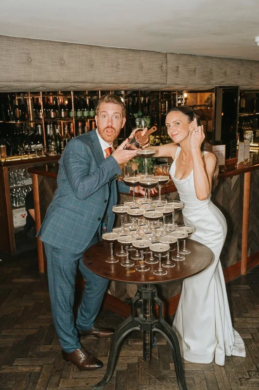  Newlyweds having fun pouring coffee martinis into a glass tower during their wedding reception at Balfour St Barts, London. 