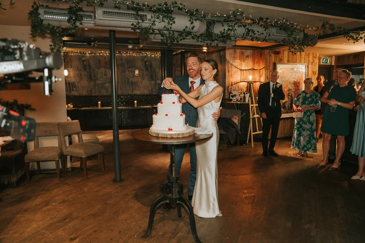  Bride and groom cutting their wedding cake during the evening reception at Balfour St Barts in Smithfield, London. 