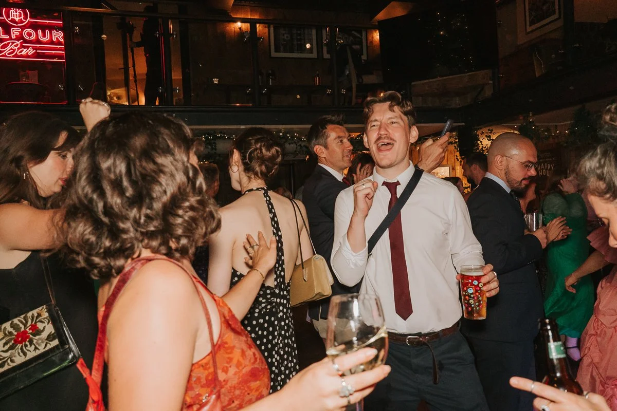  Wedding guests dancing and celebrating beneath the Balfour Bar neon sign at a Smithfield wedding reception. 