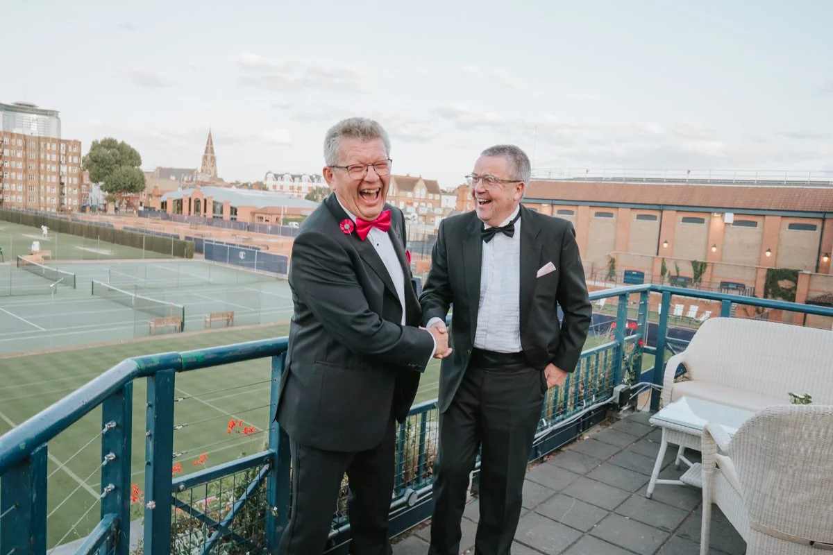  Two guests laughing together on The Queen’s Club terrace overlooking the tennis courts. 