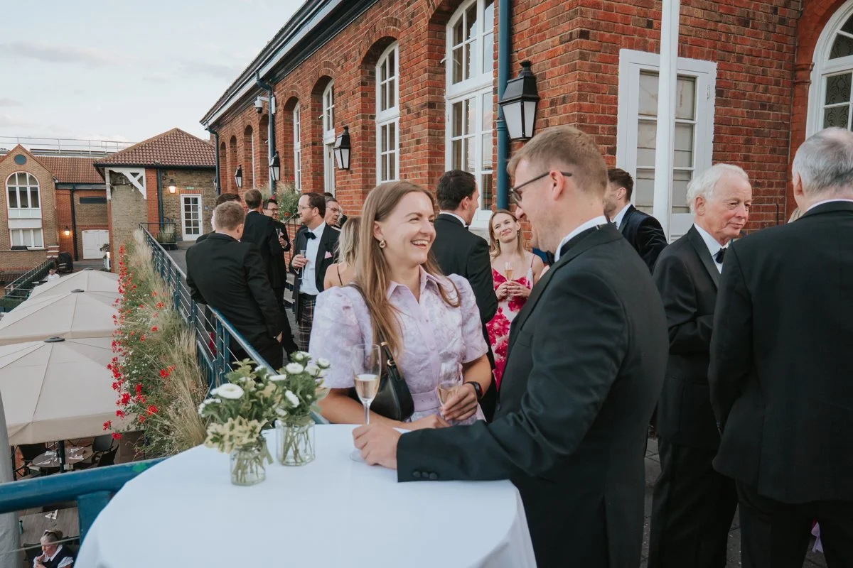  Friends chatting over drinks at an outdoor birthday reception at The Queen’s Club in West London. 