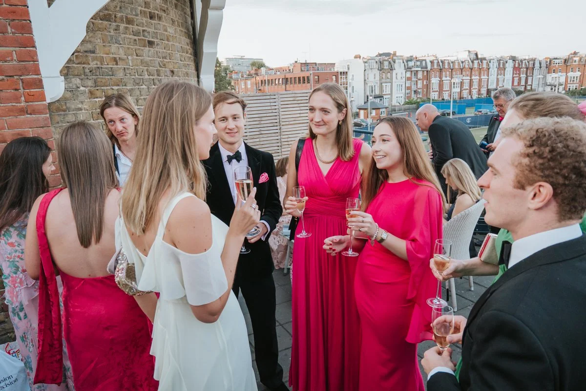  Elegantly dressed guests enjoying an outdoor drinks reception at The Queen’s Club in West Kensington. 