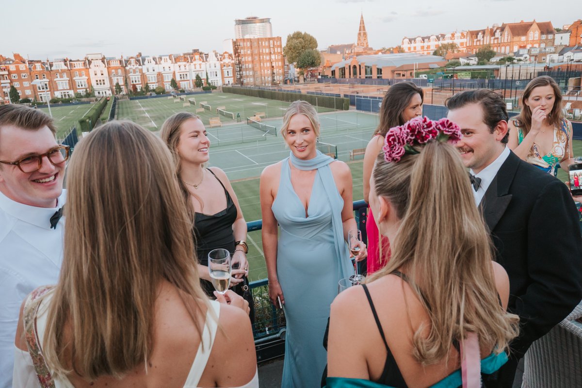  Friends socialising with champagne on the terrace overlooking the tennis courts at The Queen’s Club 