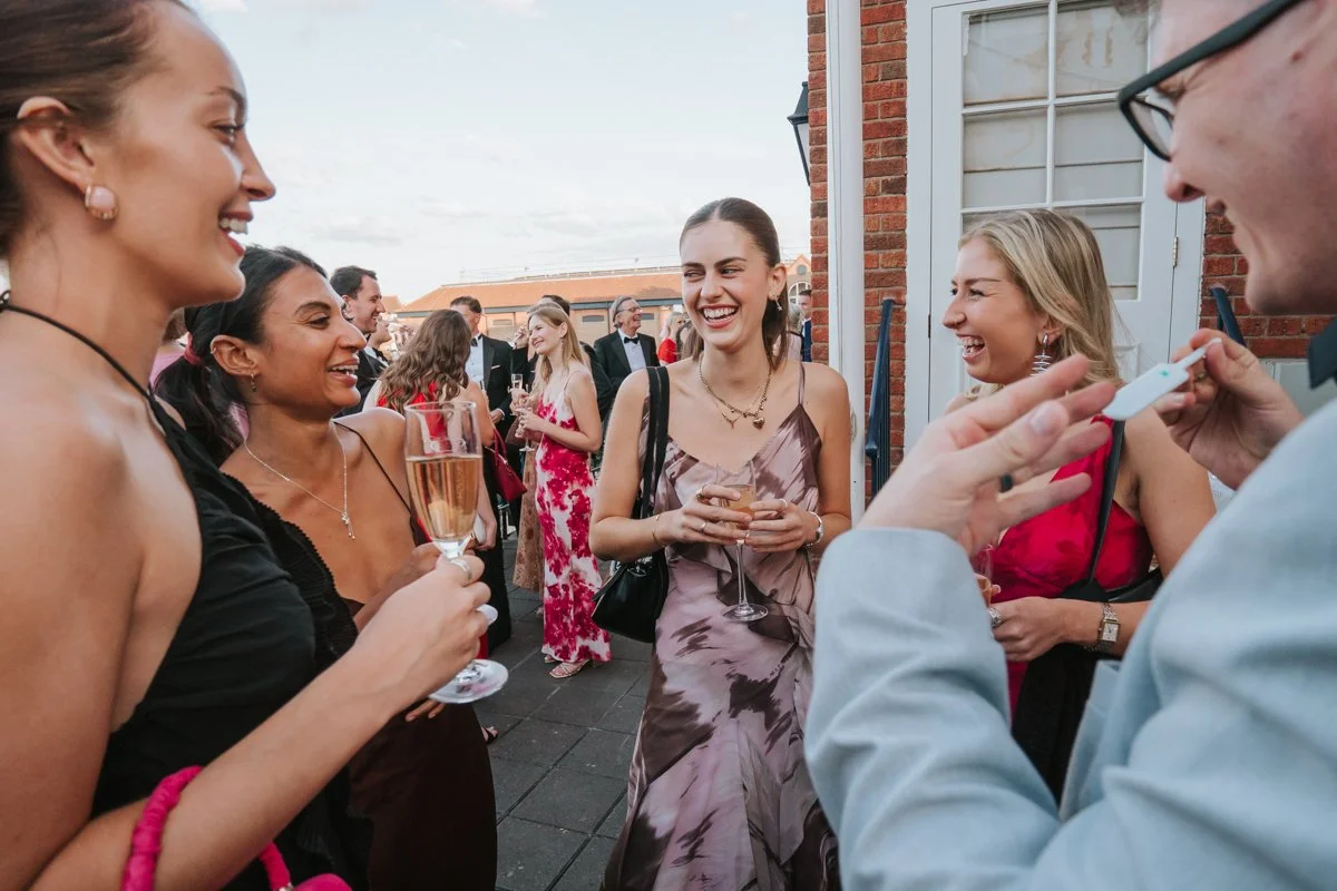  Friends chatting over drinks at an outdoor birthday reception at The Queen’s Club in West London. 
