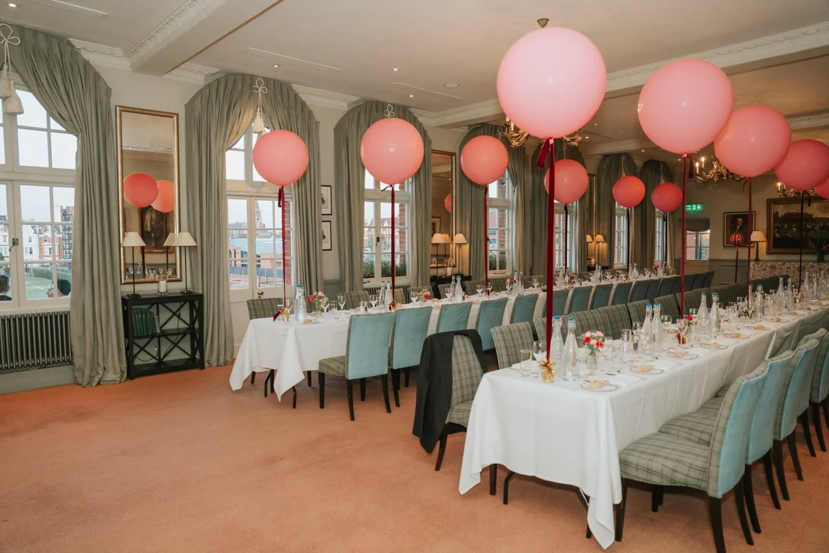  Private dining room at The Queen’s Club set for a 30th birthday meal with pink balloons and long dining tables. 