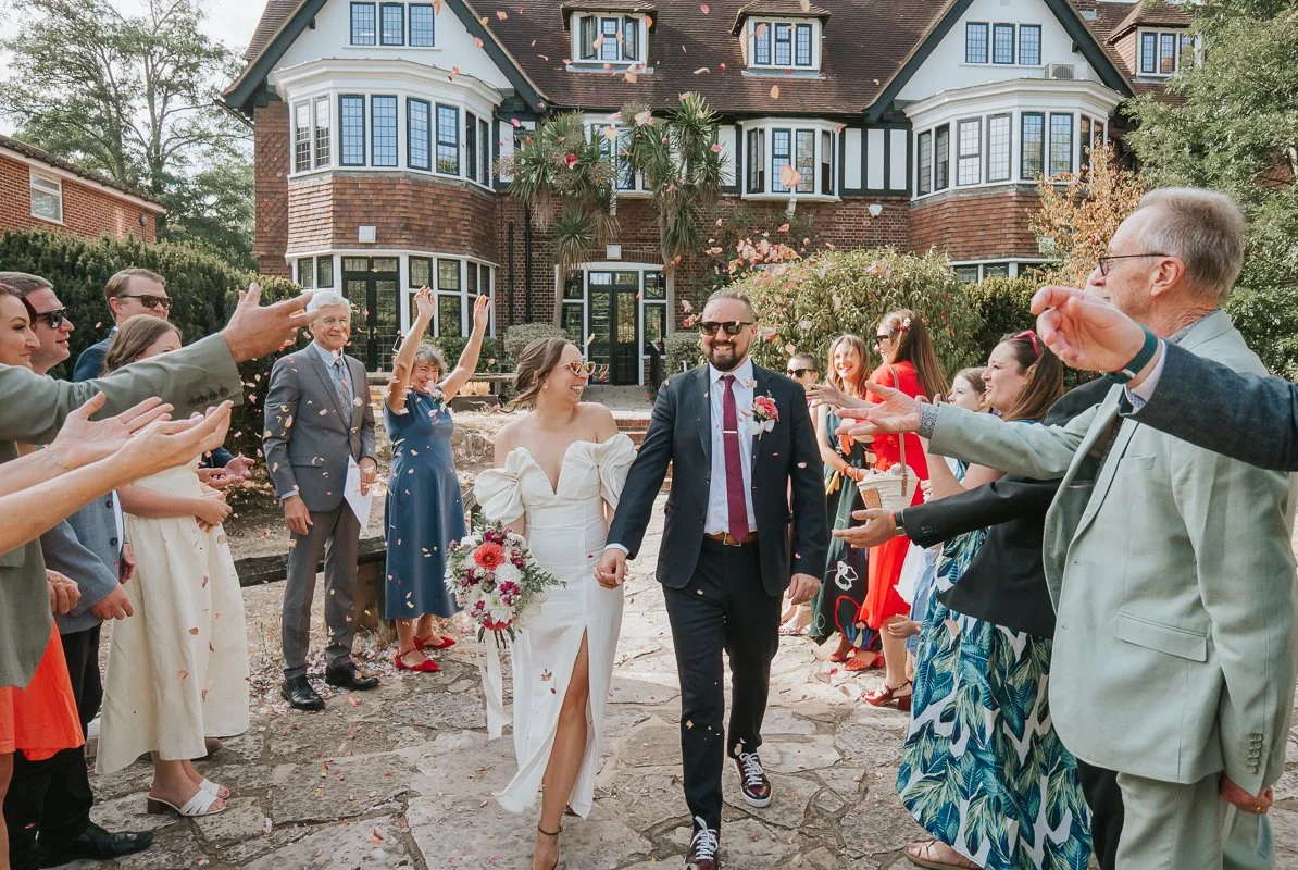  Newlyweds walking through confetti and cheering guests outside Weybridge Register Office after their wedding ceremony. 