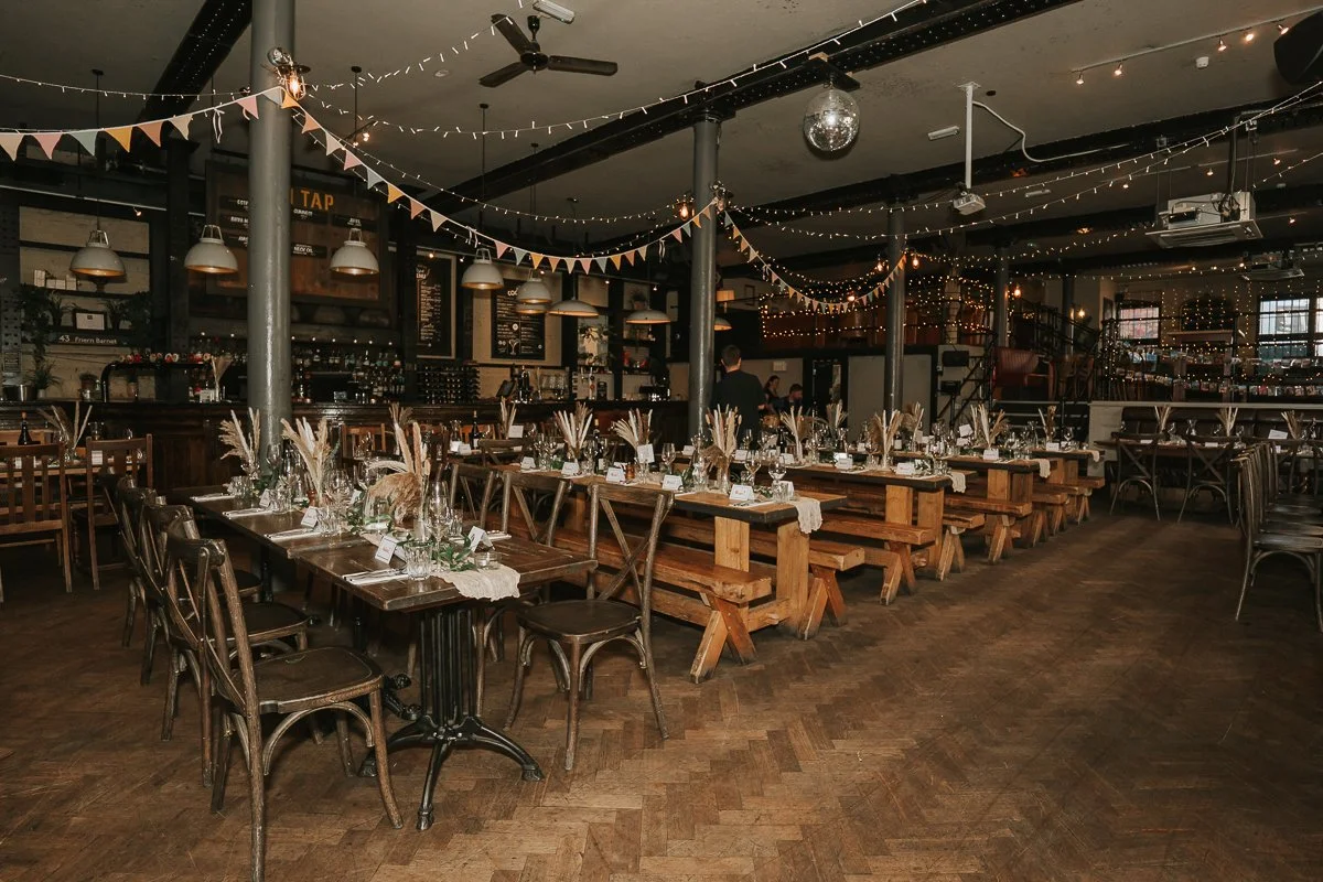  The Depot in Islington dressed for a wedding reception with long wooden tables, flowers and festoon lights. 