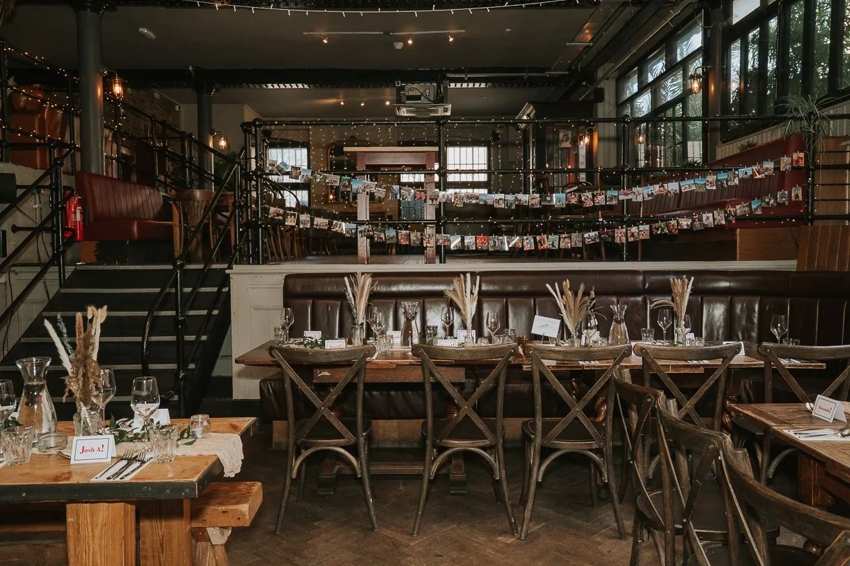  Wedding breakfast set-up inside The Depot in Islington, with rustic tables, floral details and photographs decorating the venue. 