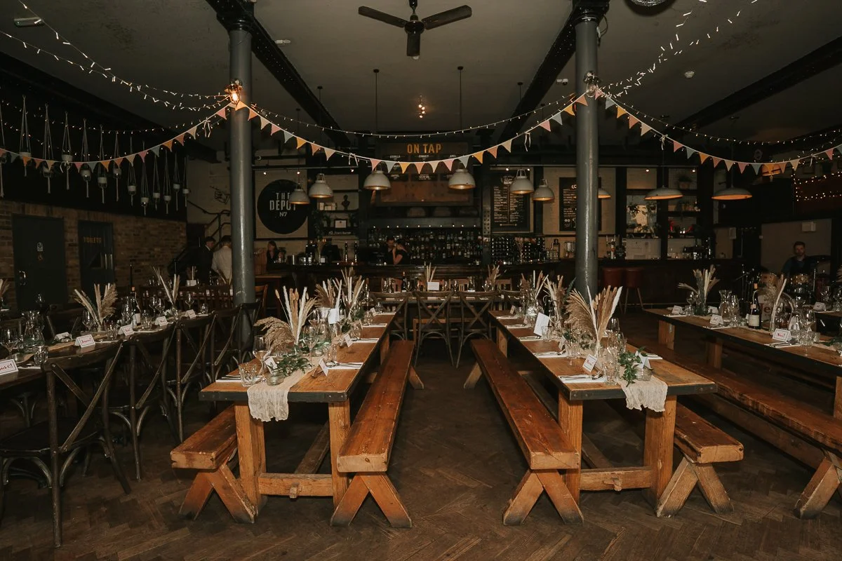  The Depot in Islington dressed for a wedding reception with rustic wooden tables, bench seating and festoon lights. 
