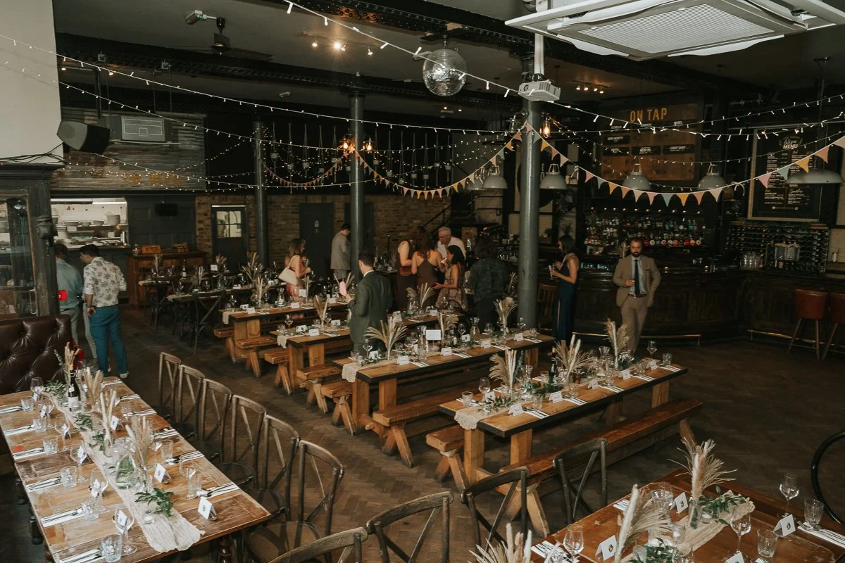  The Depot in Islington dressed for a wedding reception with rustic long tables, festoon lights and dried flower arrangements. 