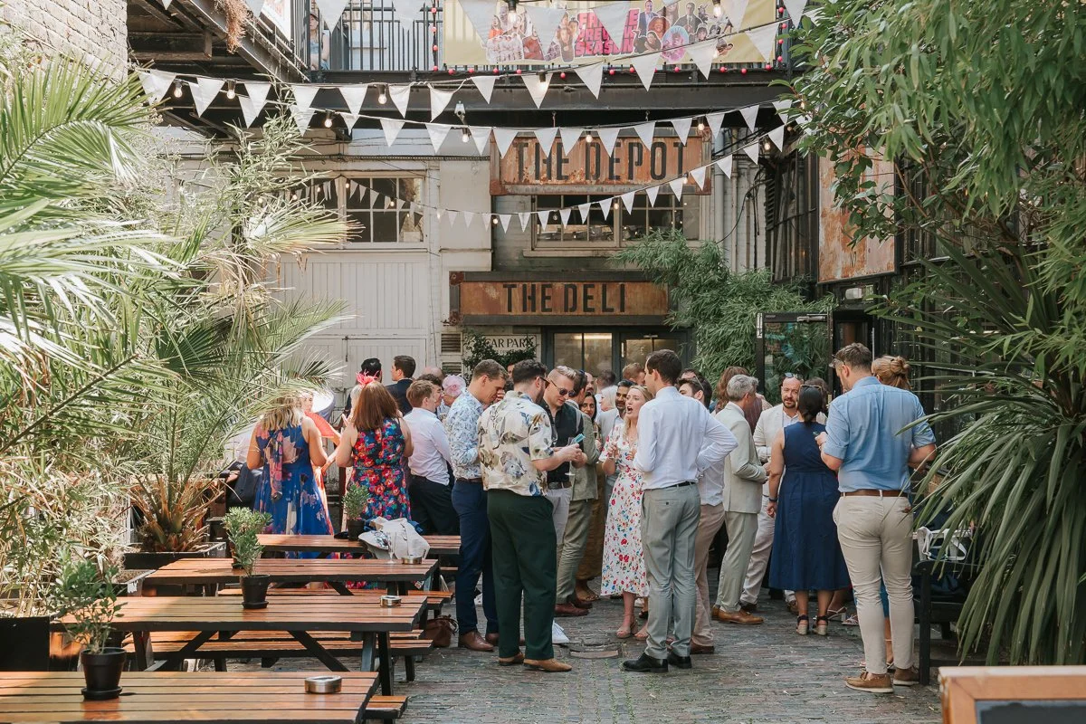  Wedding guests enjoying drinks in the outdoor courtyard at The Depot wedding venue in Islington, London. 