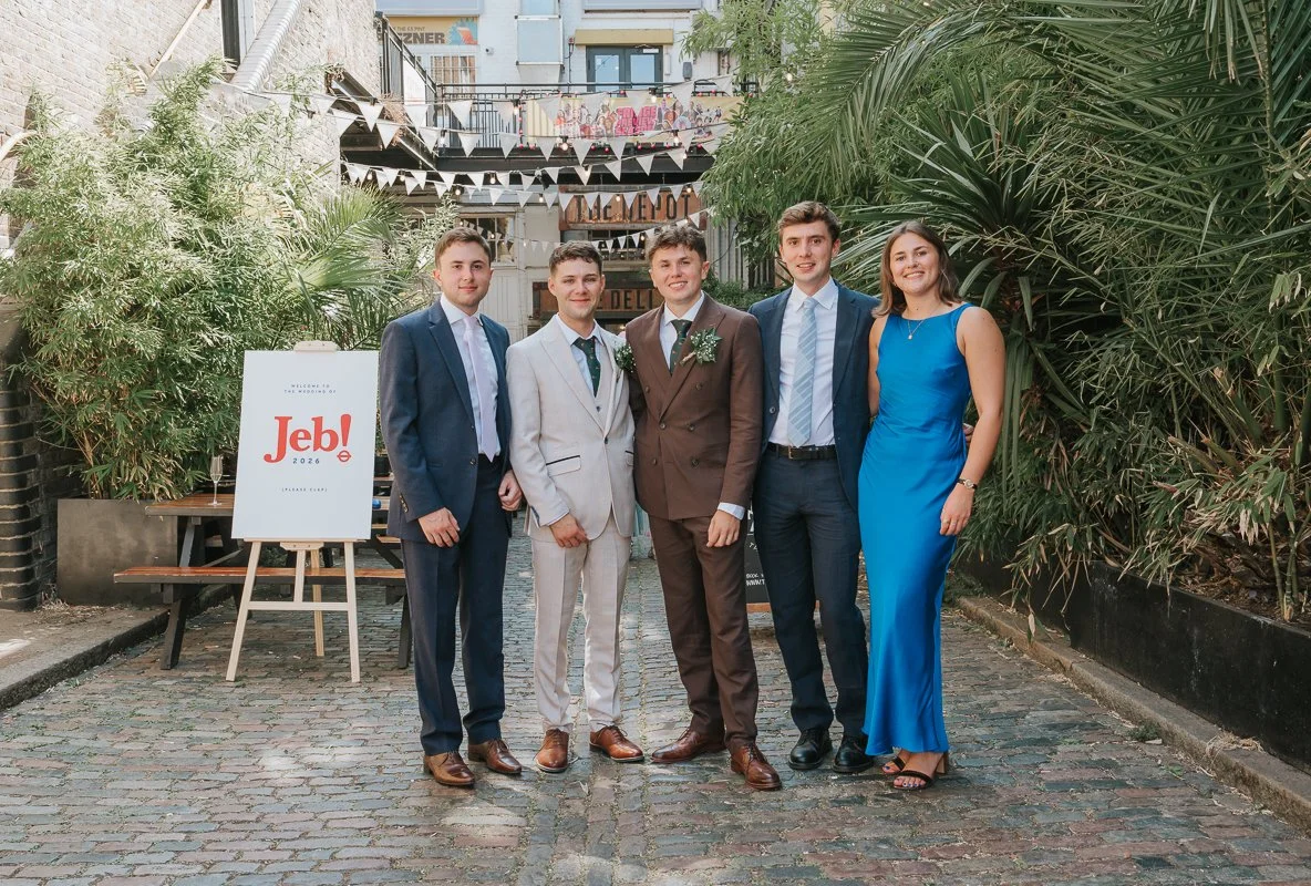  Groom and friends posing for a group photograph in the courtyard at The Depot during an Islington wedding reception. 