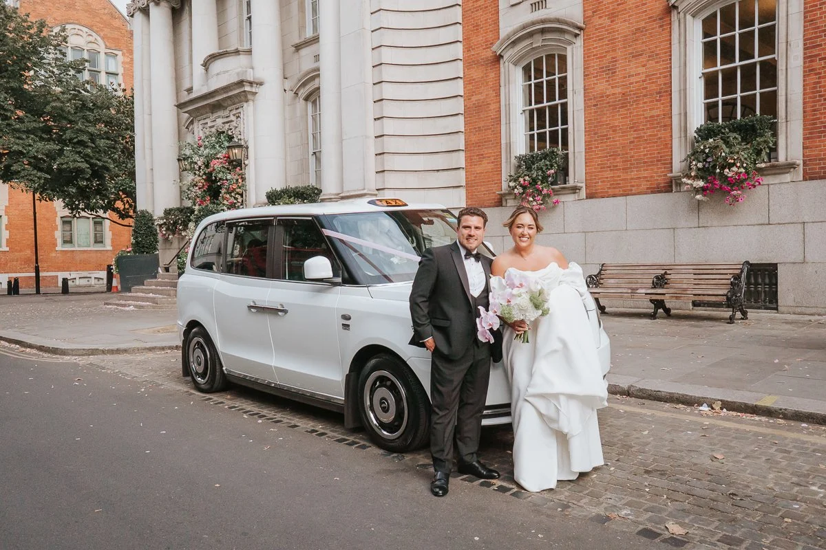  Bride and groom outside Chelsea Old Town Hall with a classic London black cab after their wedding ceremony. 