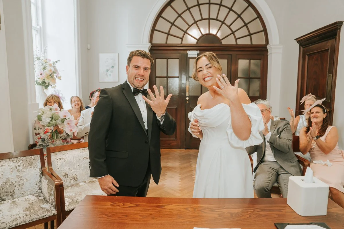  Chelsea Old Town Hall wedding photography capturing the newlyweds proudly showing their wedding rings after their ceremony, surrounded by applauding guests. 