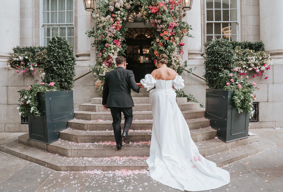  Chelsea Old Town Hall wedding photography of the newlyweds walking up the iconic steps beneath the colourful floral entrance after their ceremony. 