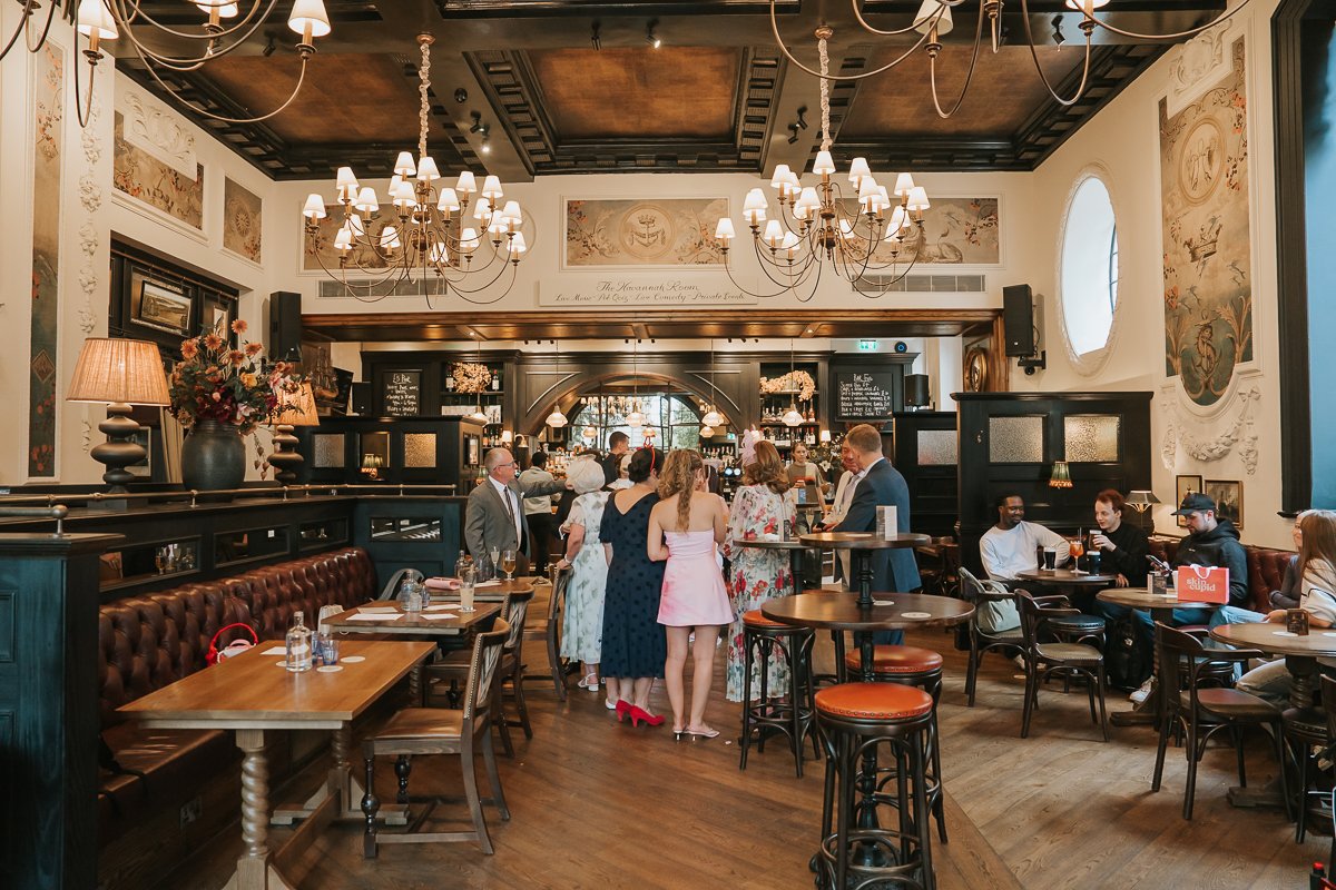  Spacious wedding reception interior at The Trafalgar on the King’s Road, with chandeliers, leather seating and a traditional wooden bar. 