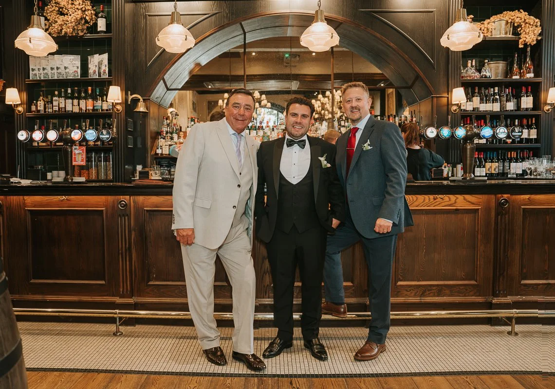  Groom posing with two wedding guests in front of the bar at The Trafalgar pub in Chelsea. 