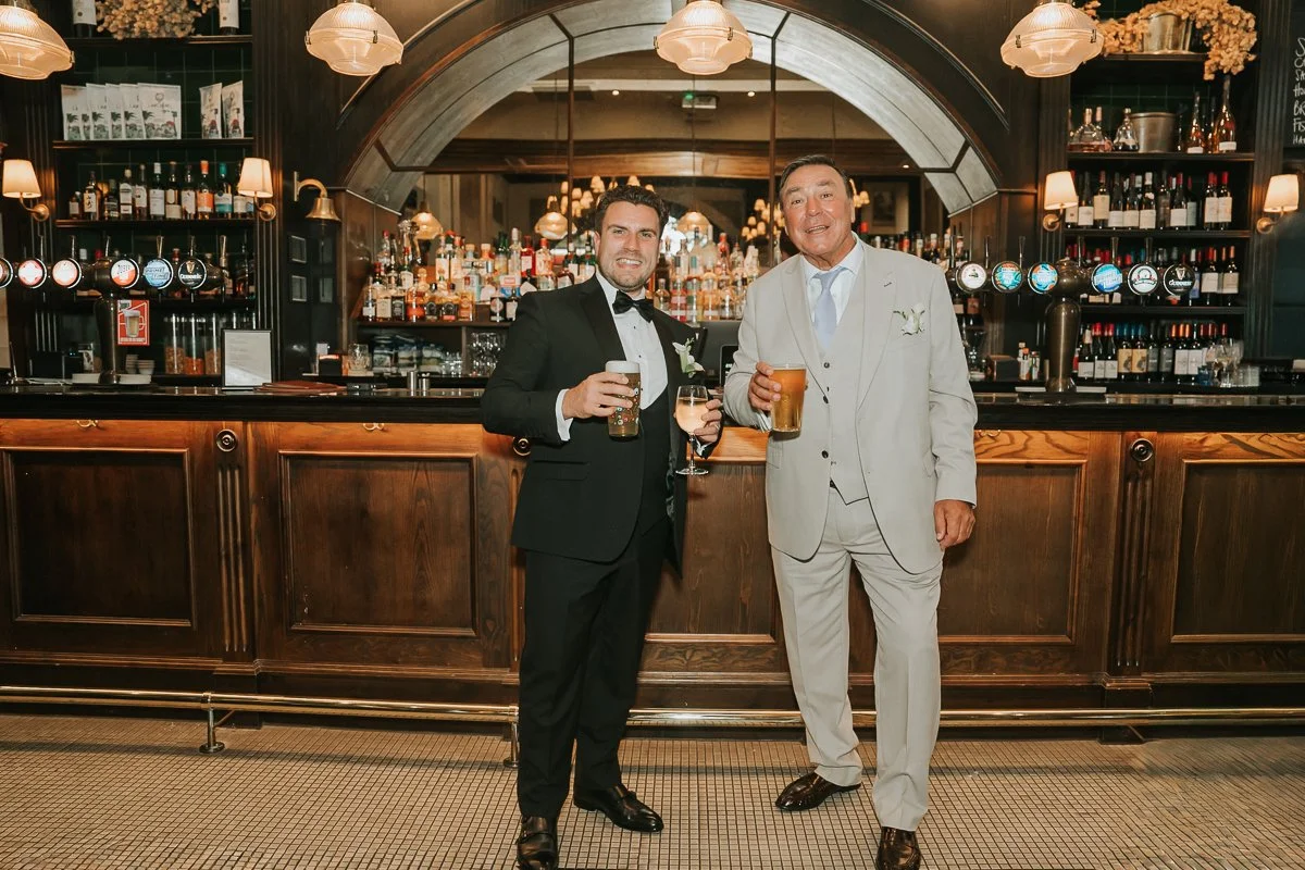  Groom and wedding guest enjoying drinks together at the traditional wooden bar in The Trafalgar. 
