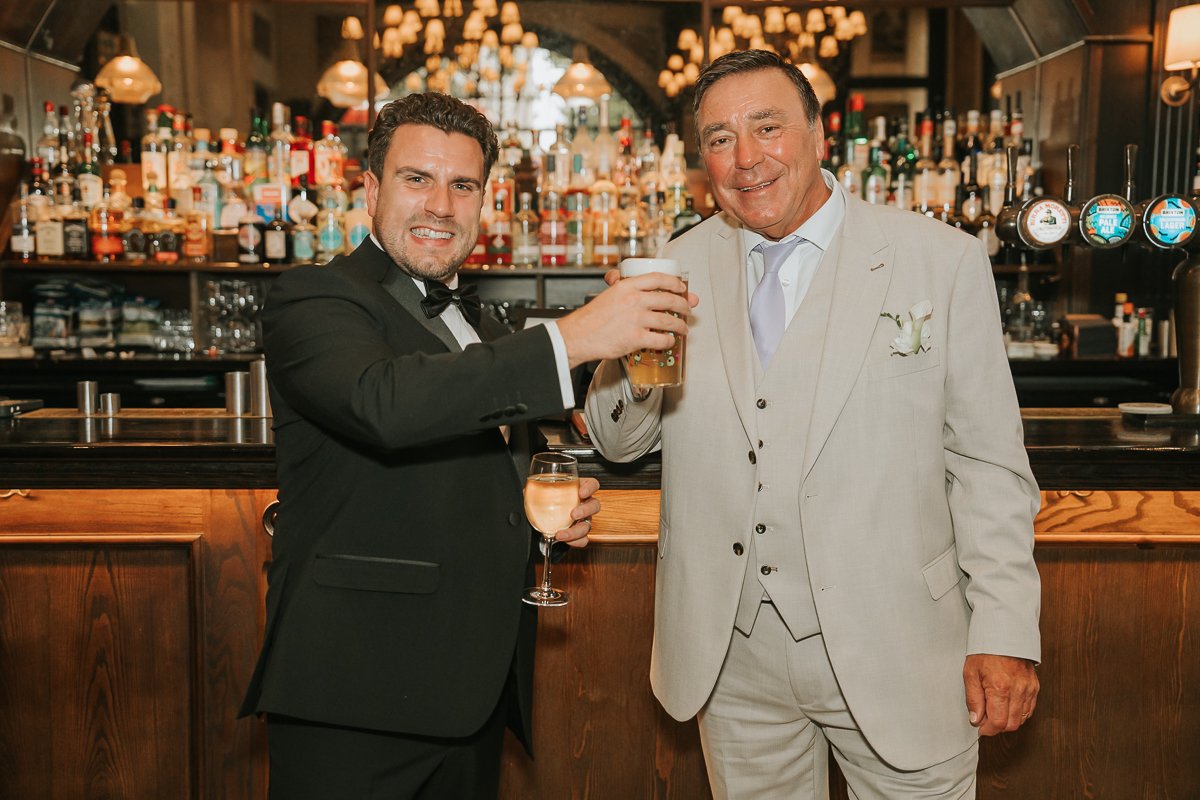  Groom raising a glass with a wedding guest during their relaxed Chelsea pub wedding reception. 