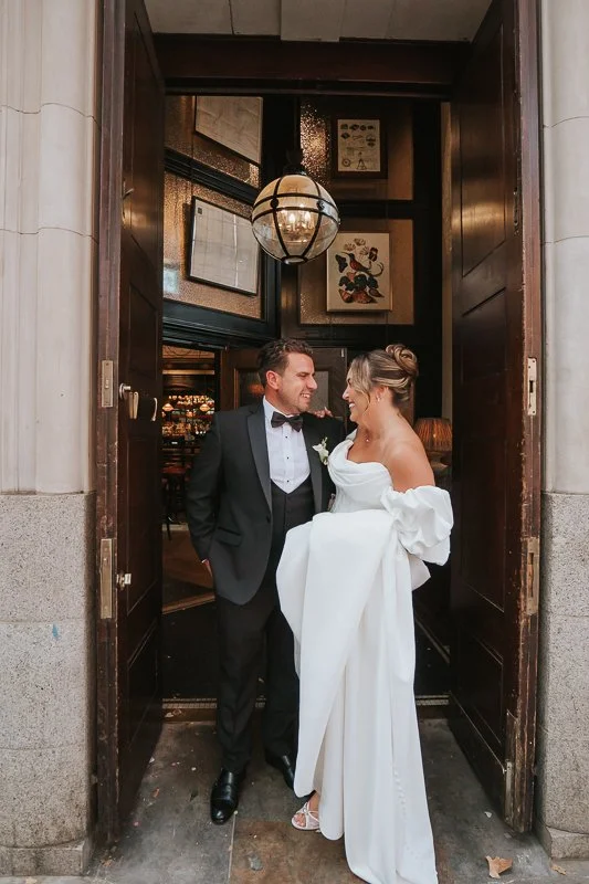  Newlyweds smiling at one another in the grand doorway of The Trafalgar Chelsea. 