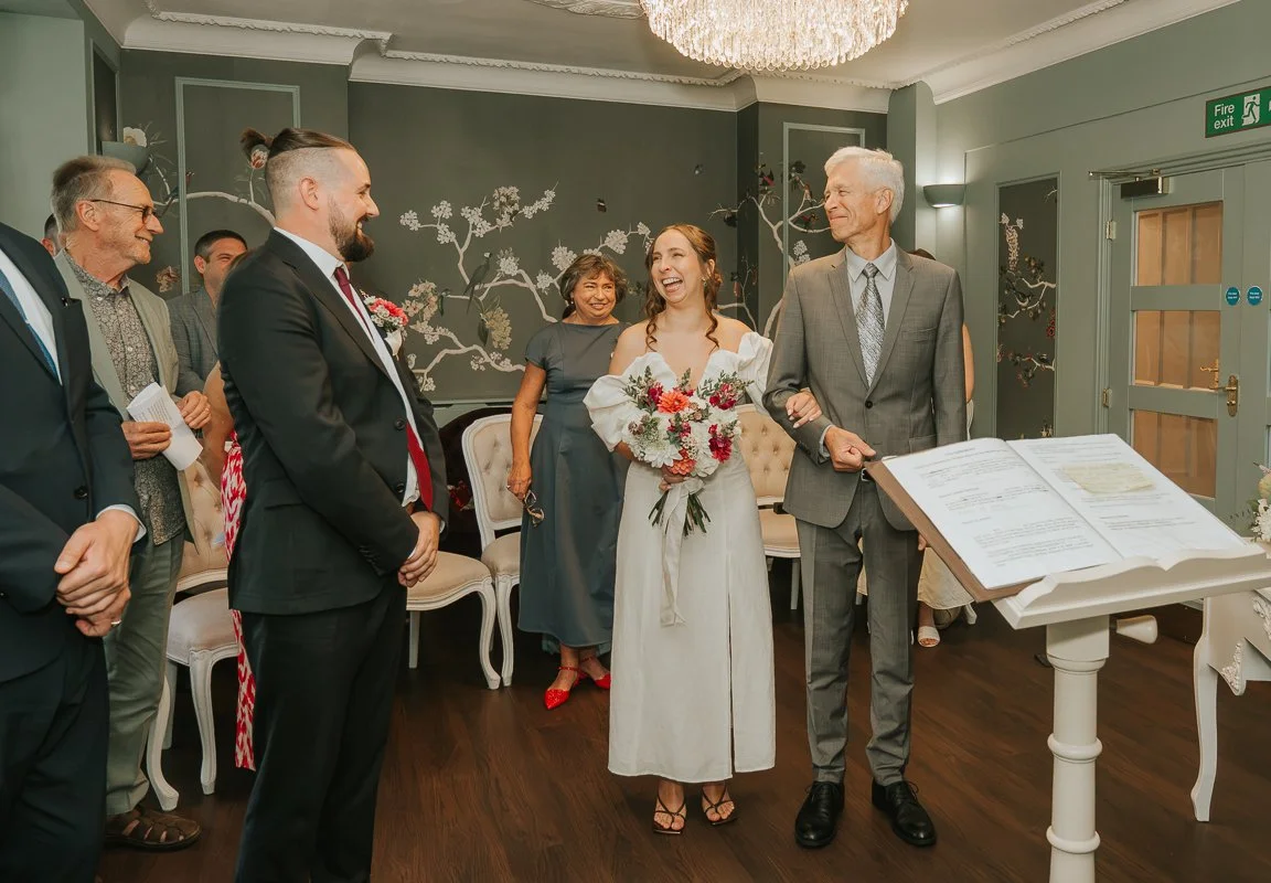  Bride walking into her wedding ceremony at Weybridge Register Office with her father, as the groom looks on. 
