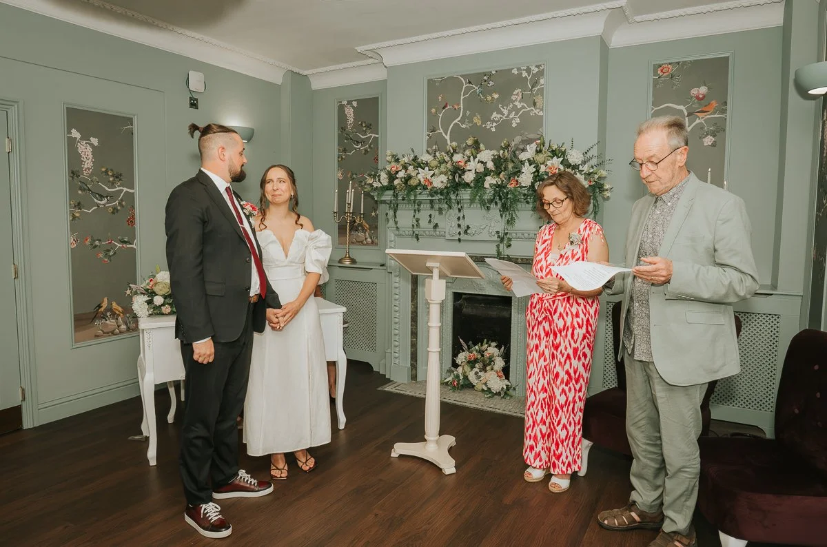  Bride and groom listening to a reading during their wedding ceremony at Weybridge Register Office. 