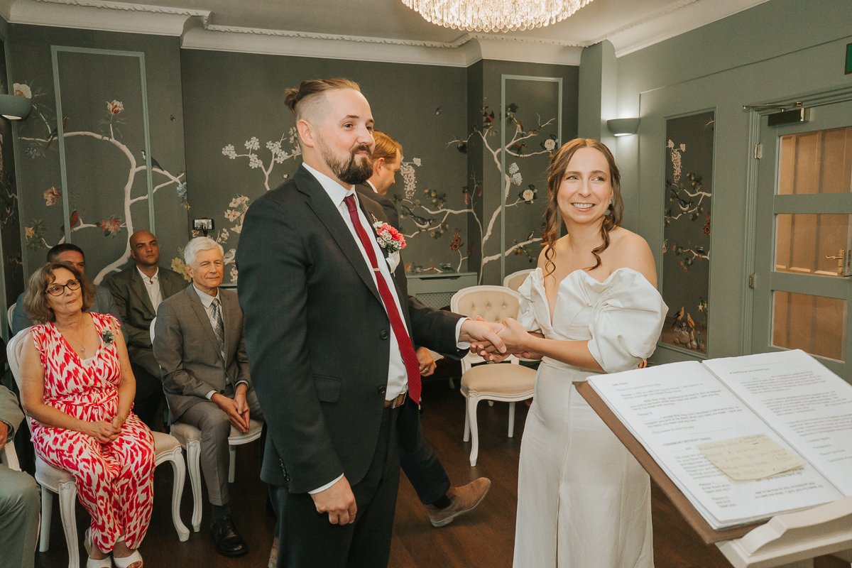  Bride and groom holding hands during their wedding ceremony at Weybridge Register Office in Surrey. 