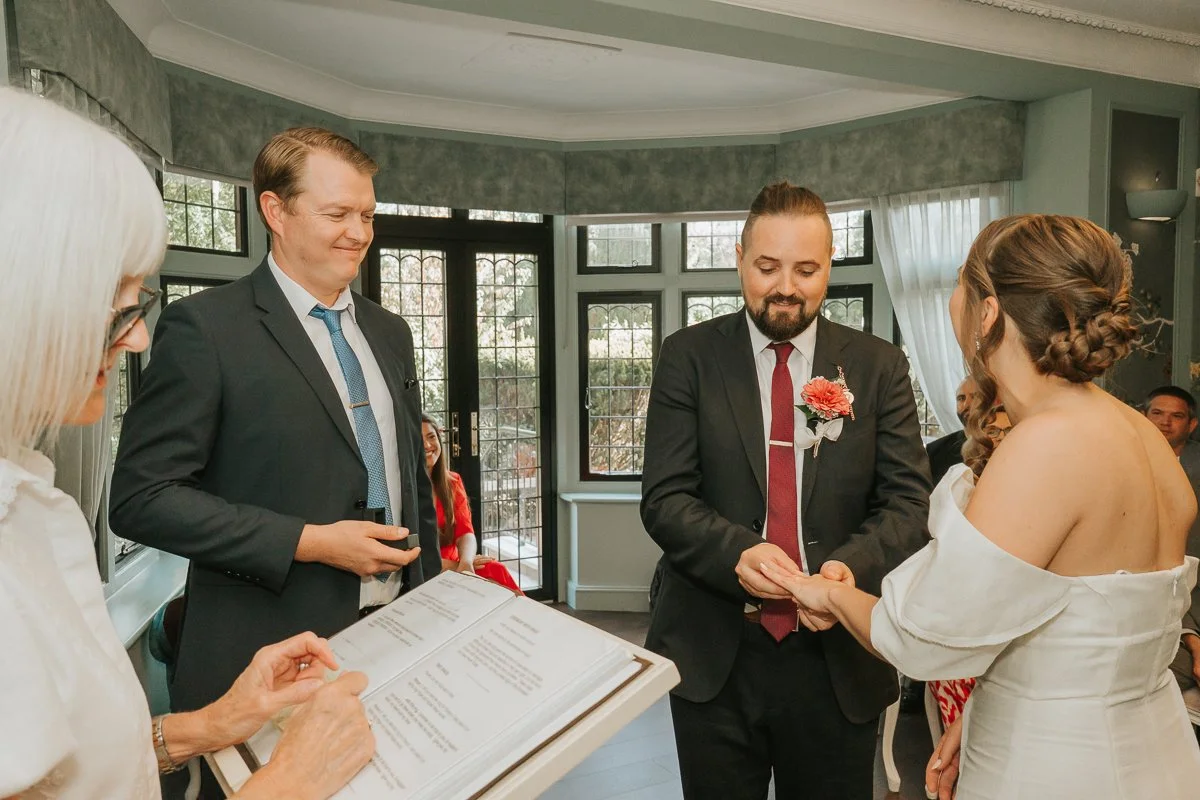  Groom placing the wedding ring on his bride’s finger during their ceremony at Weybridge Register Office. 