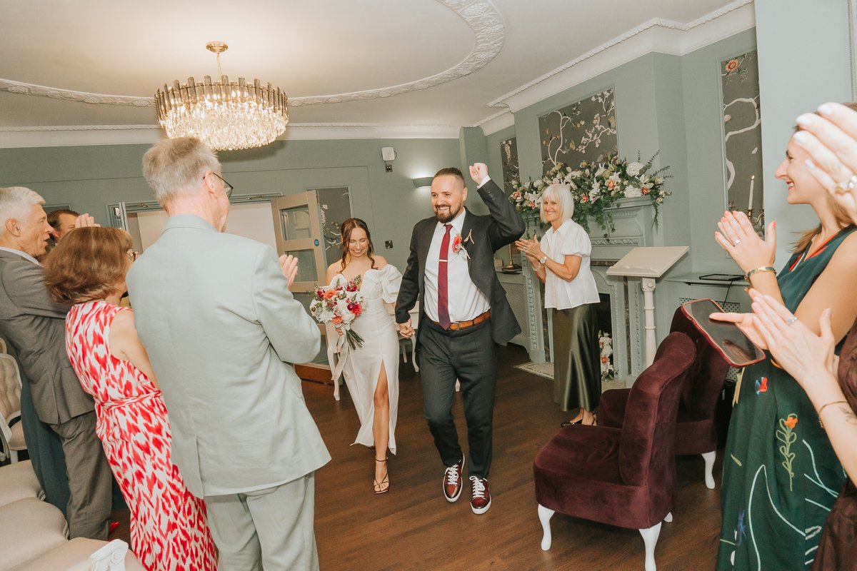  Newly married couple walking through their cheering guests after their wedding at Weybridge Register Office. 