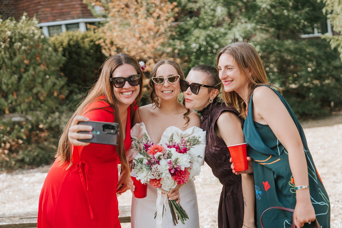  Bride taking a selfie with friends in the gardens after her wedding ceremony at Weybridge Register Office. 