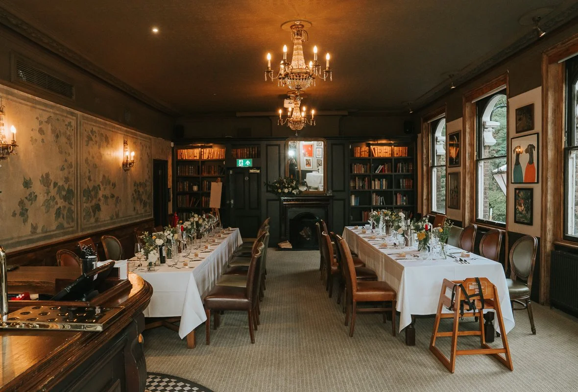  Bridge Room at The Prince Albert set for a wedding meal, with long tables, chandeliers and a fireplace. 