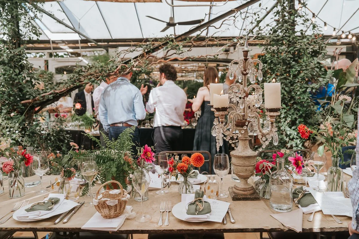  Wedding breakfast table decorated with colourful flowers, ferns and an ornate candleholder in the Central Greenhouse at Petersham Nurseries. 