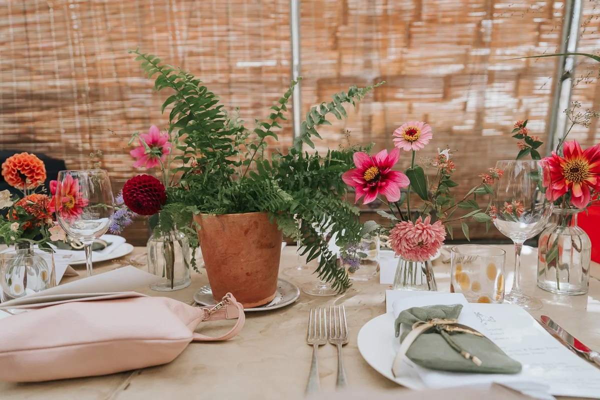  Potted fern and colourful dahlias in glass vases decorating a wedding table at Petersham Nurseries, Richmond. 