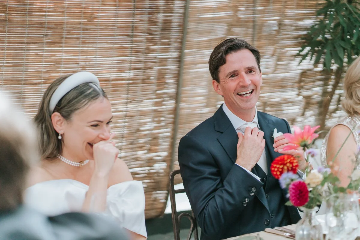  Bride and groom laughing together during their wedding breakfast at Petersham Nurseries, Richmond 
