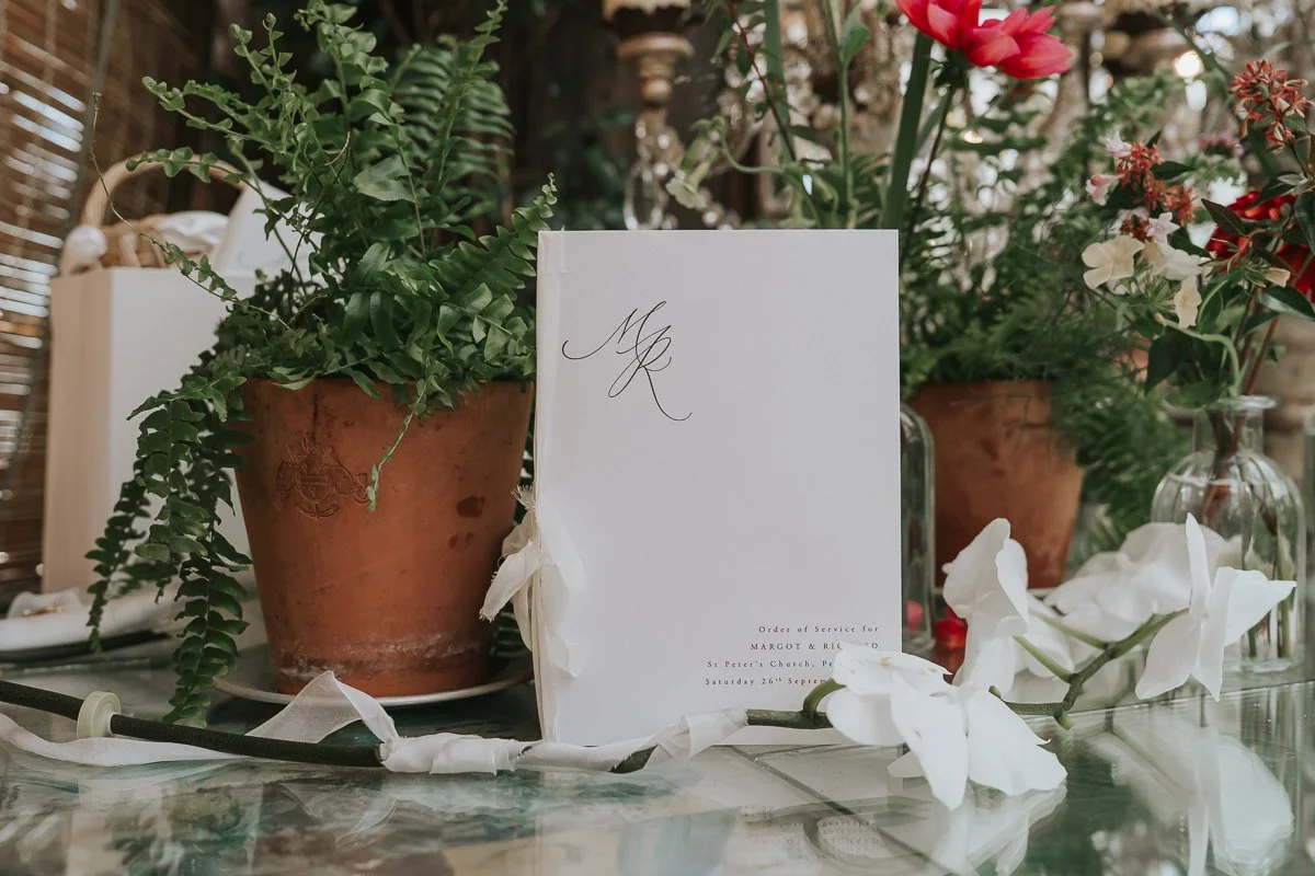  Wedding order of service displayed beside a potted fern and white orchids at Petersham Nurseries. 