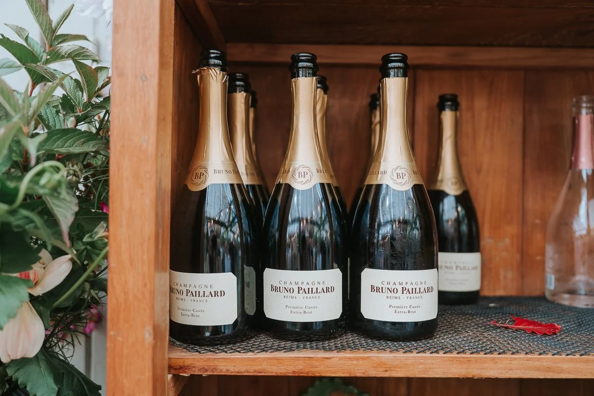  Bruno Paillard Champagne bottles arranged on a wooden shelf beside foliage in the Central Greenhouse at Petersham Nurseries. 