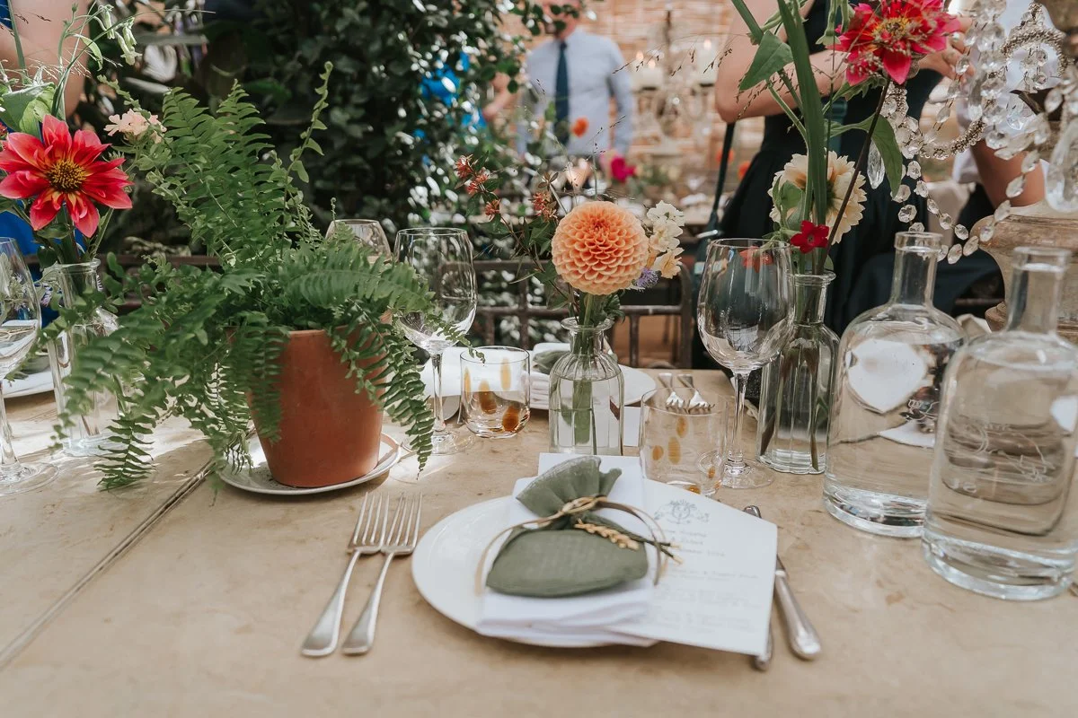  Wedding place setting with a green favour bag, potted fern and colourful dahlias at Petersham Nurseries. 