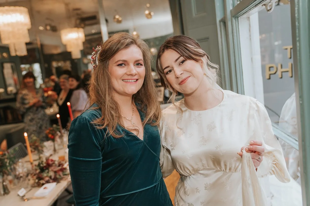  Bride and guest smiling together beside a window at The Phene during a Chelsea pub wedding reception. 