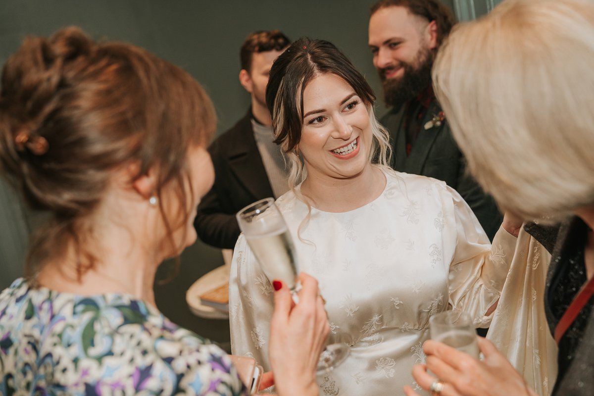  Bride chatting with guests holding sparkling wine during her wedding reception at The Phene, Chelsea. 