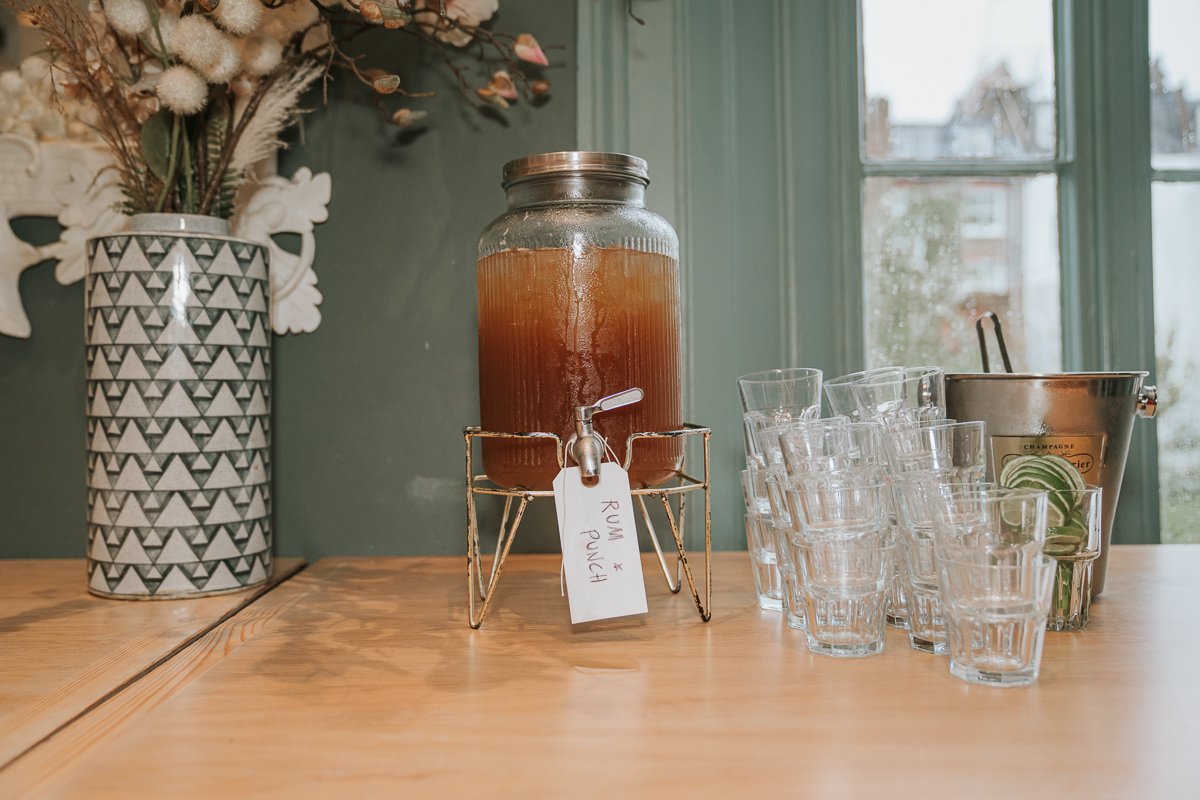  Rum punch dispenser with glasses and sliced lime ready for wedding guests at The Phene. 